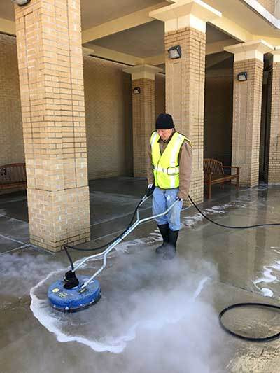 Image of Priority Exterior Cleaning, LLC. Employee Power Washing a commercial property sidewalk. Hospital and Hotel Pressure Washing Services